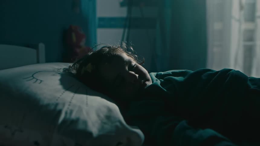 Mother carries child into the bedroom and places the sleeping boy on the bed