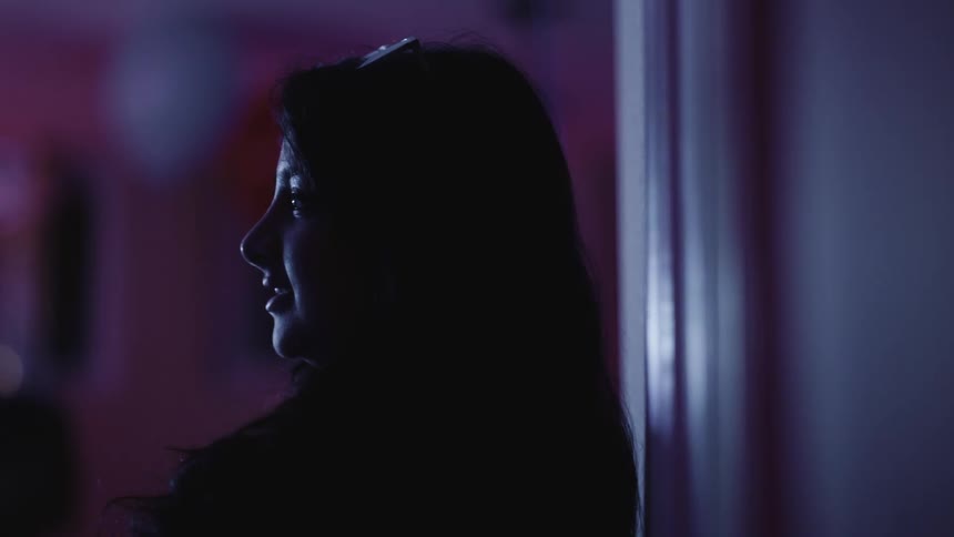 Side portrait of a young woman indoors with purple lights and low lighting