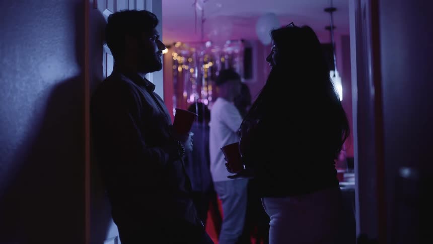 Young couple standing in a doorframe at a party talking to each other