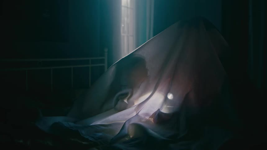 A child shines a flashlight under a bed sheet