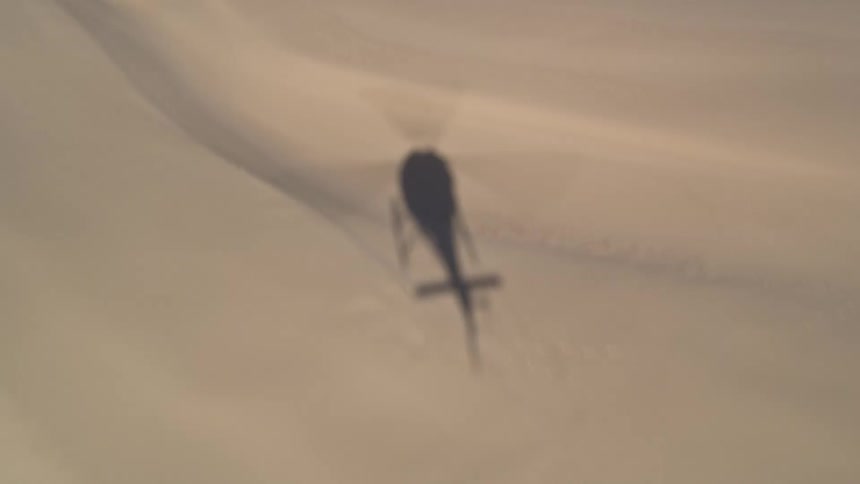 Shadow of a helicopter flying over desert dunes