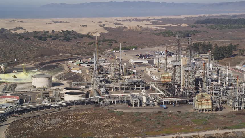 A large refinery sits near a desert and a coast
