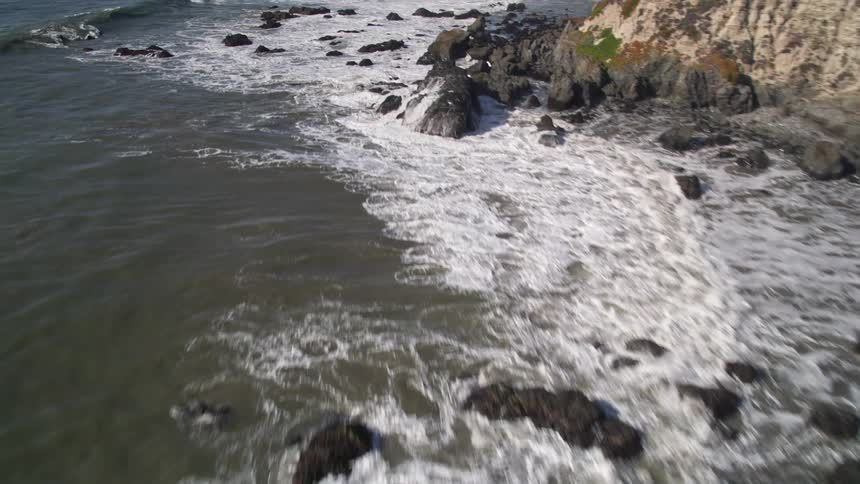 Aerial footage of a coastal shoreline with waves splashing against the rocks
