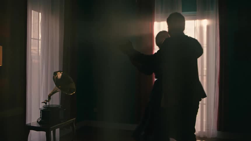 Silhouette of a man and a woman dancing together in a room with a vinyl record