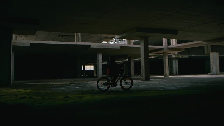 Person on bicycle rides through empty concrete structure during the day