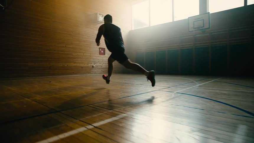 A man practices basketball on a dimly lit indoors court