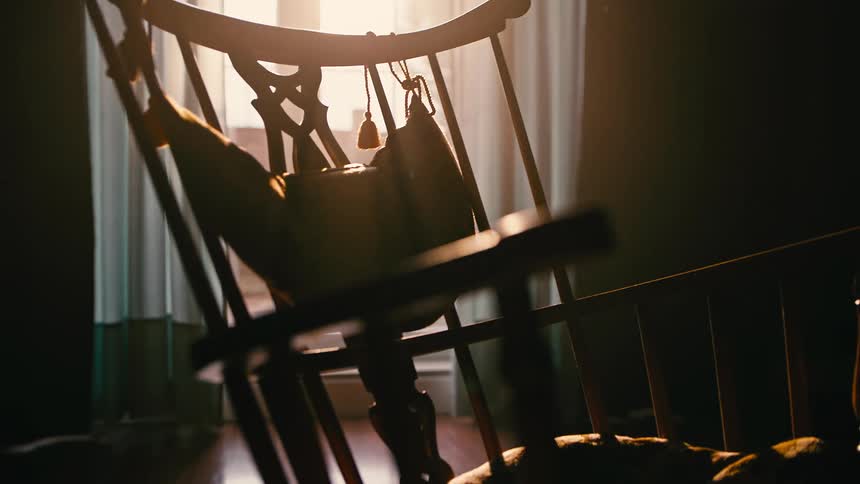 A wooden rocking chair swings in a dark room