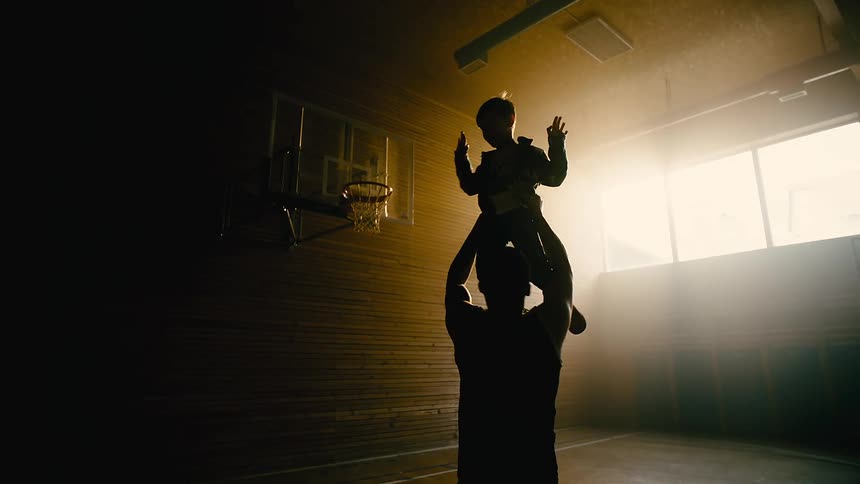 A father holds his young son as he moves around a basketball court