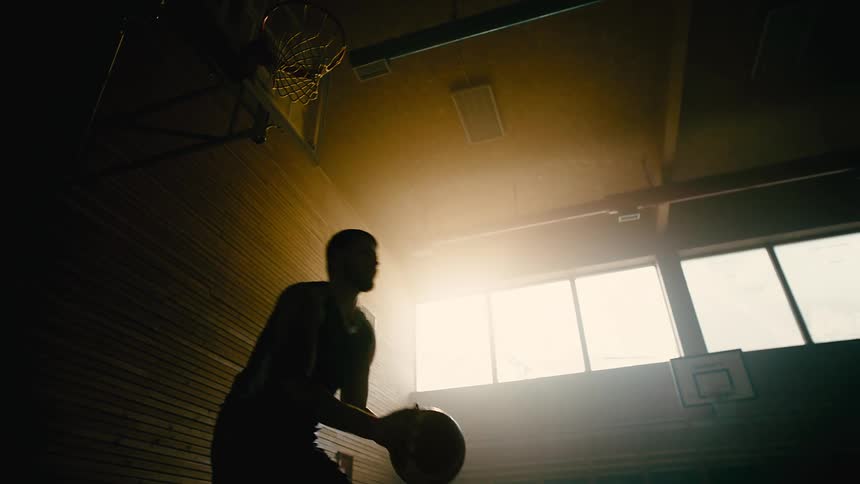 A man practices basketball on a dimly lit indoors court