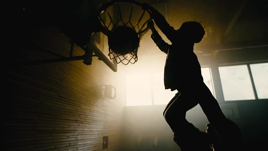 Silhouette of the father lifting his son who scores a basket with a basketball inside an indoor court