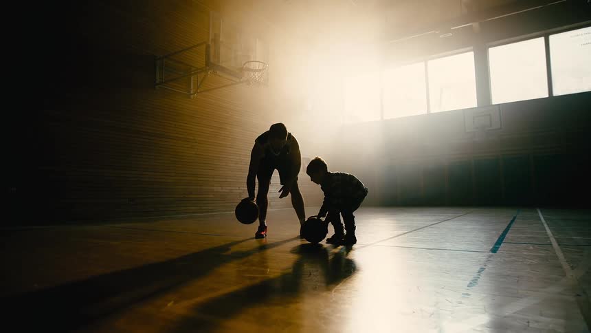 Silhouette of father and son on a court hitting the basketball on the ground