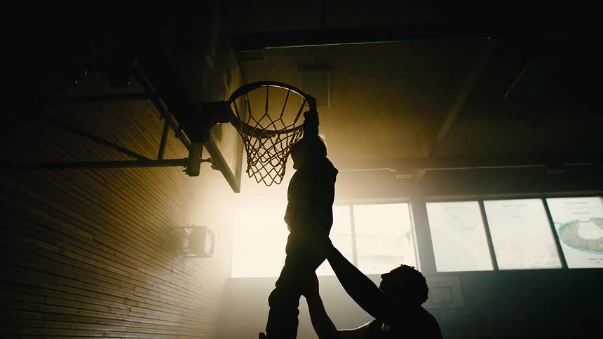 Father and son practicing basketball on a dimly lit indoors court