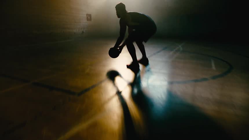 A man practices basketball on a dimly lit indoors court