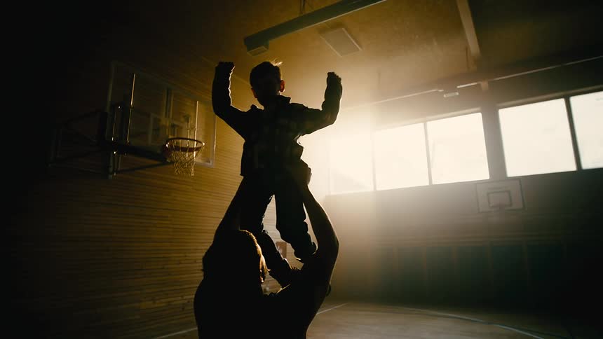 Father lifting his son and spinning with him while they are on a basketball court