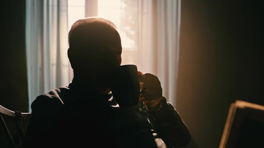 Silhouette of a man sitting in a rocking chair reading and holding a mug that emits smoke