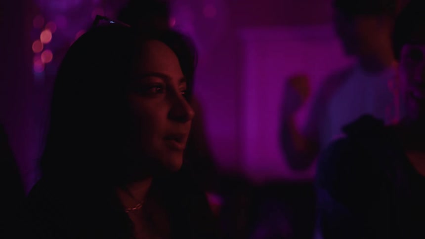 Close up of the face of a woman under purple lighting talking at a party