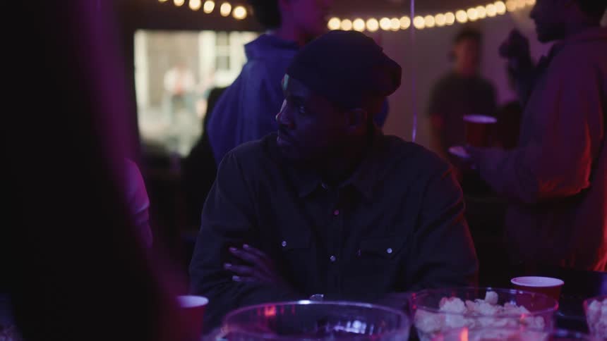 A young man is socializing with friends at a small party a tv is on in the background