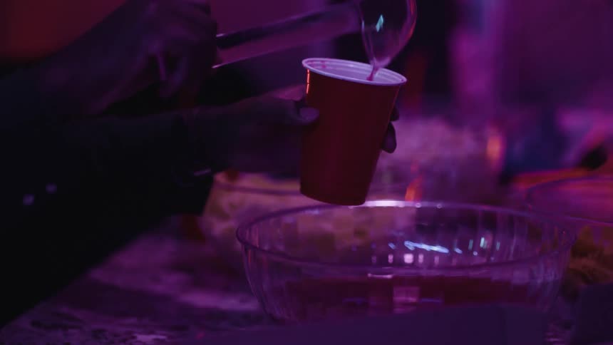 Close up of a person serving punch on a red plastic cup at a party