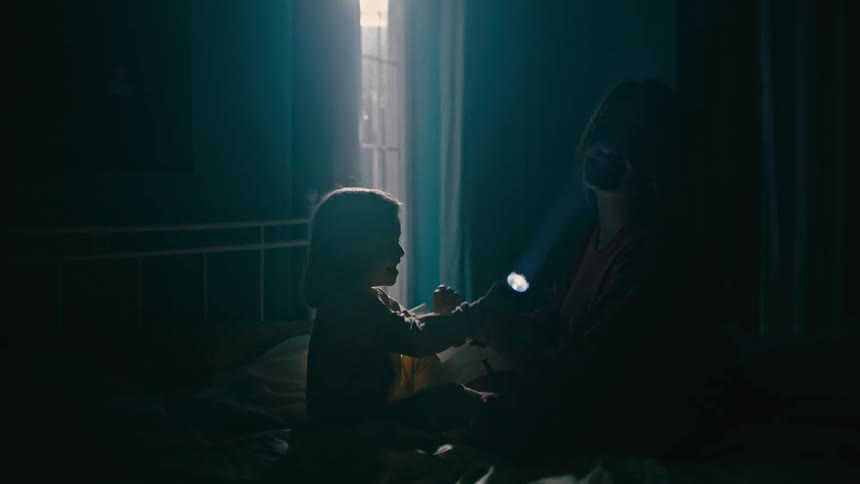 Mother and child sitting on a bed playing with a flashlight in the dark