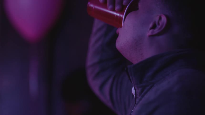 Side portrait of a young man drinking a drink from a red disposable cup
