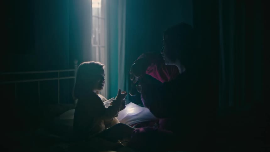 Mother sitting with her daughter on the bed playing with a flashlight