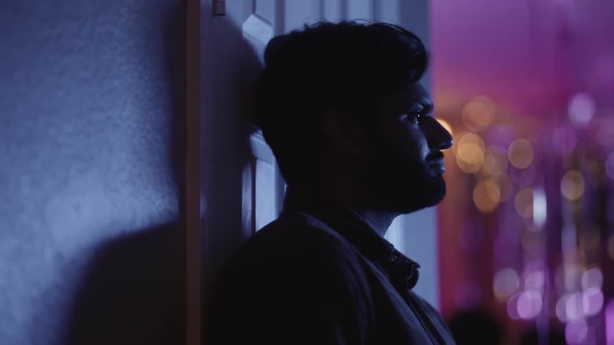 Close up of the face of a man under purple lighting talking at a party