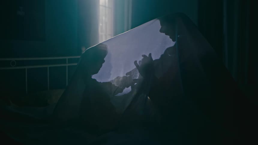 An adult and a child playing on a bed under a sheet