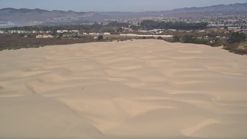A helicopter flies over a desert near a coastal city