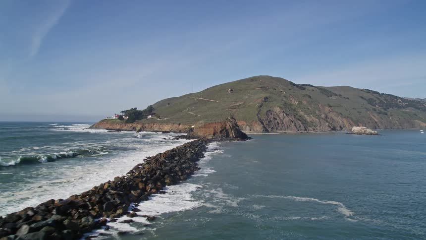 Aerial panorama of a rocky trench dividing the ocean and mountains in the background during a blue sky day