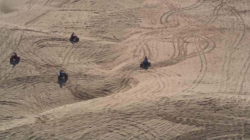 People ride four wheelers leaving tracks on extensive sands near beach