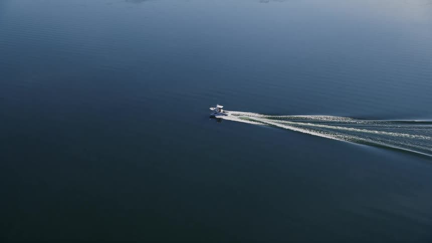 Boat sails across the water near the coast leaving a splashing trail behind as it moves