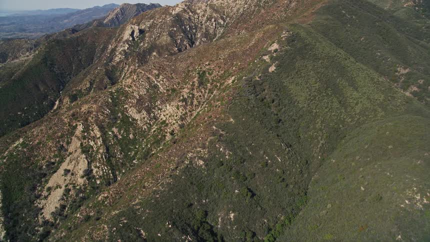 Aerial panorama of mountain ranges with cliffs and vegetation on a blue sky day