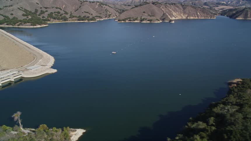 Aerial view of a large reservoir surrounded by hilly terrain and a dam