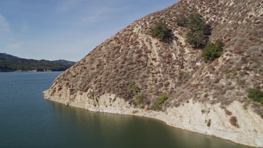 Boat moves through the water between a promontory and a forested shore