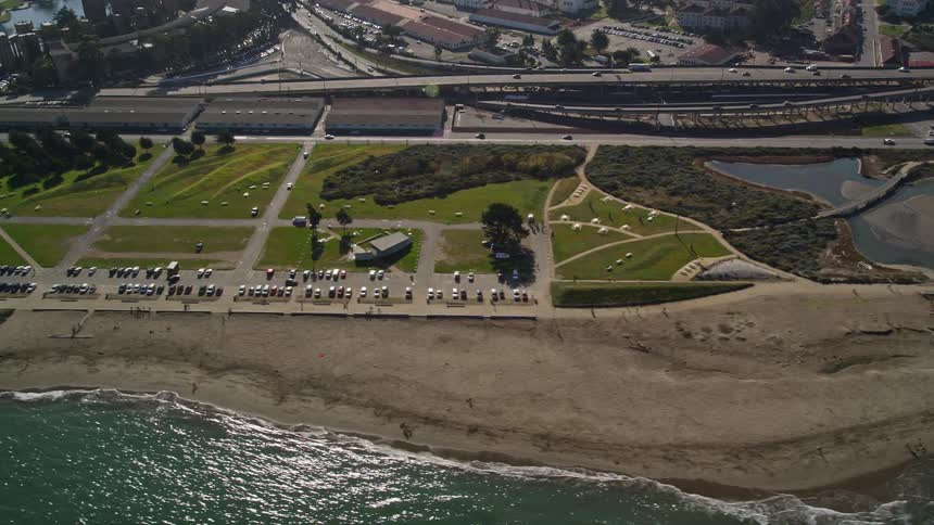 Traffic flows along roads passing buildings and marina bordering the ocean