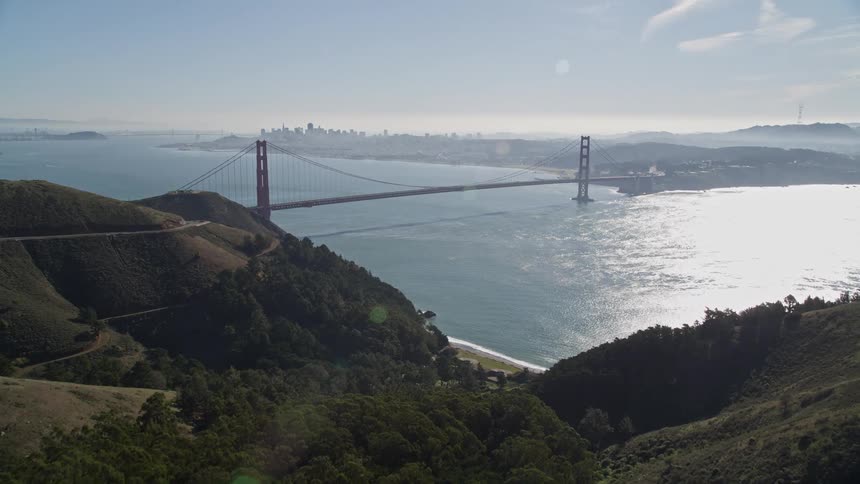 Aerial panorama of mountains overlooking a bridge over the sea and a metropolis on the horizon