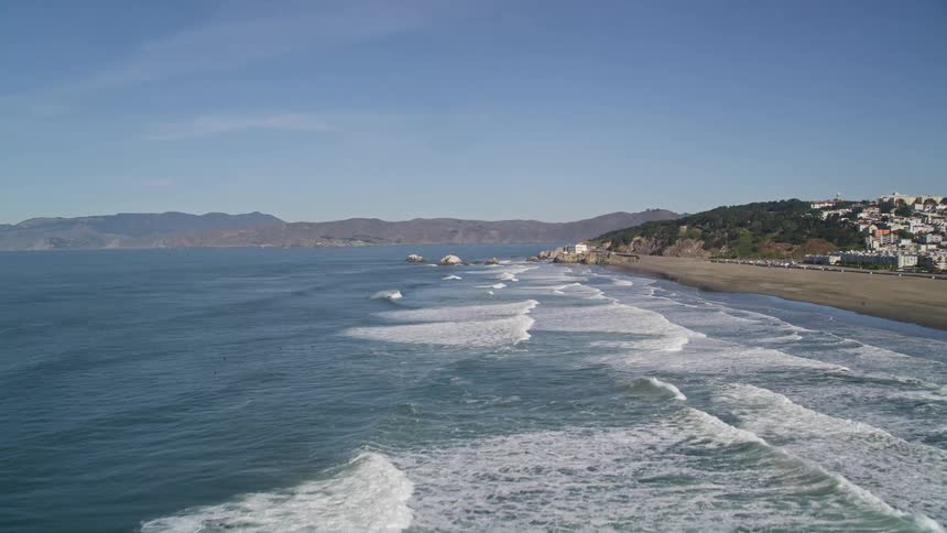 Panorama of an extensive sea with waves at the edge of the coast with an urban city on a blue sky day