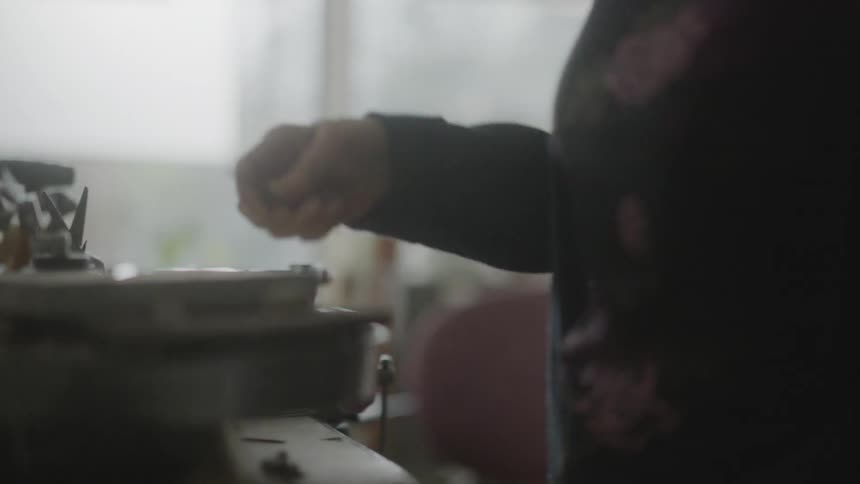 Older woman uses a torch to craft an item at a workbench
