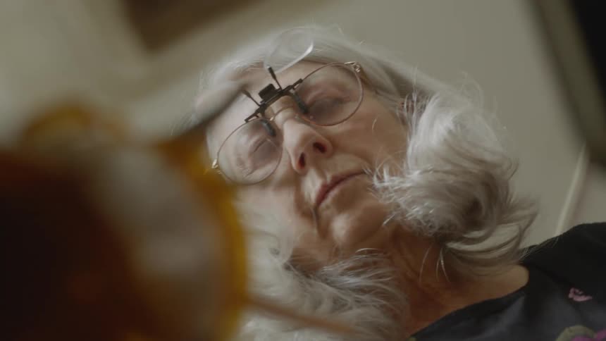 Elderly woman wearing magnifying glasses picks up a brush from a cardboard box