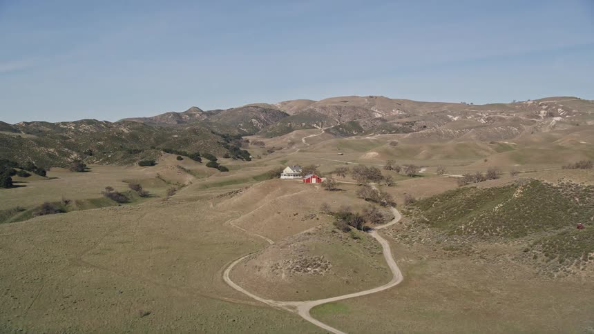 Aerial view of a house and a red barn over a hill in the countryside