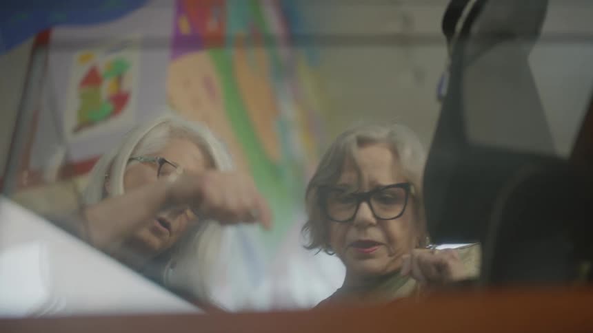 Two women gesture and talk indoors