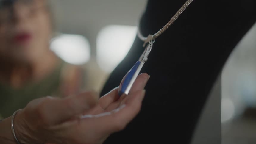 A hand showcases an elegant necklace with a blue gem
