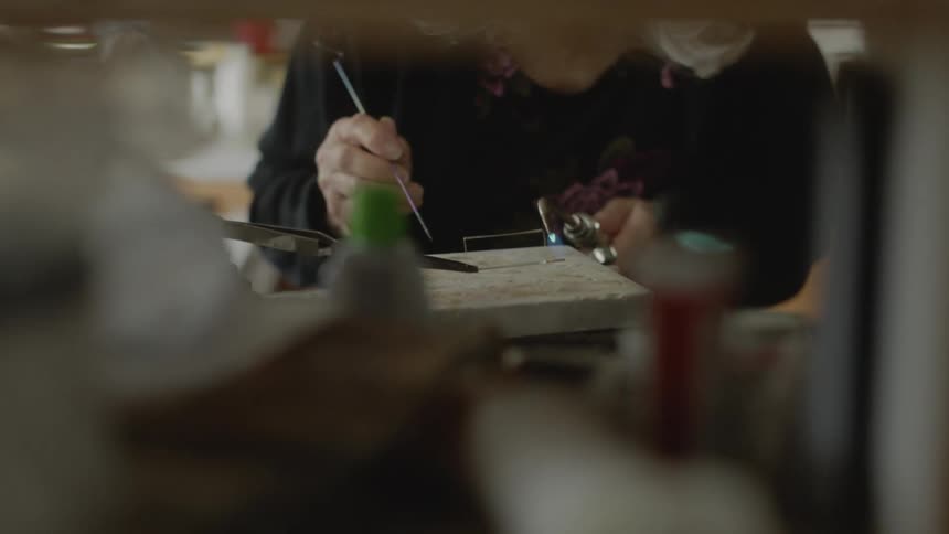 A ladys hands holding a torch and a needle and welding an abstract metal rod