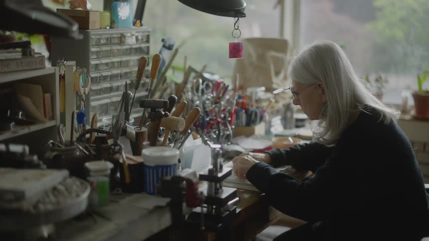 Lady sitting at an office table using tools and working with a metallic object in silver