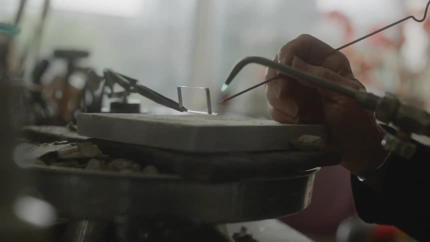 Hands of a woman with a blowtorch welding a small silver object