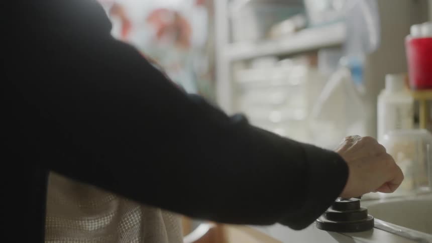 Close up of an elderly woman cleaning utensils in the sink