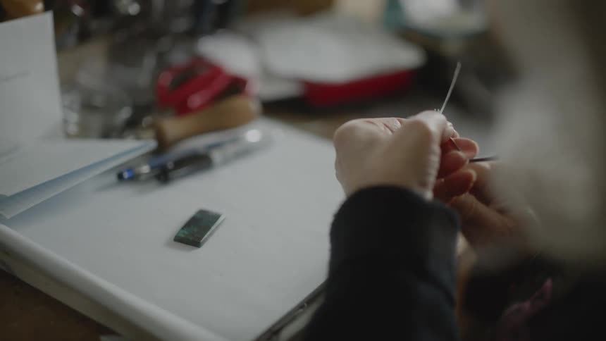 Hands of an elderly woman with pliers making a mold in a thin metal