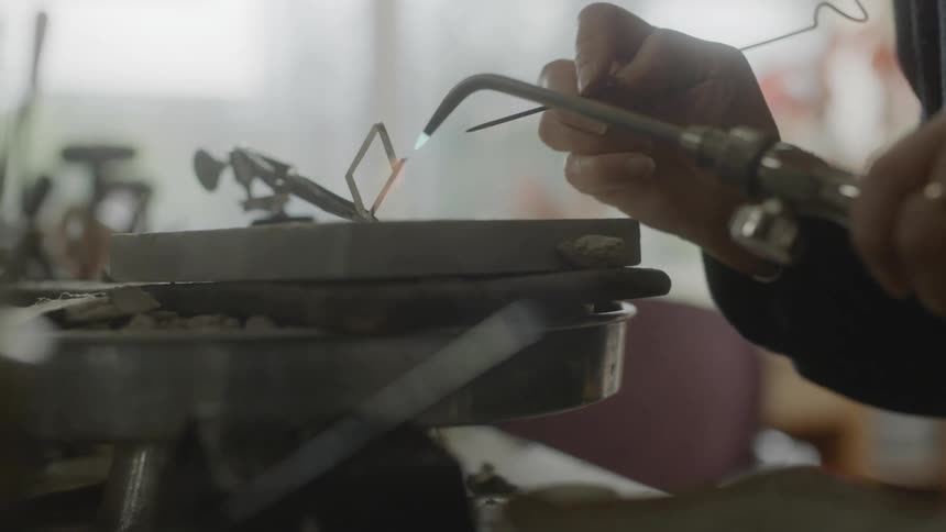 Hands of a woman with a blowtorch welding silver metal