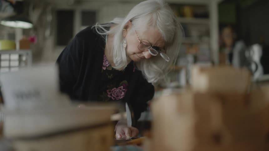 Elderly woman with a hammer hammering a small sheet of metal