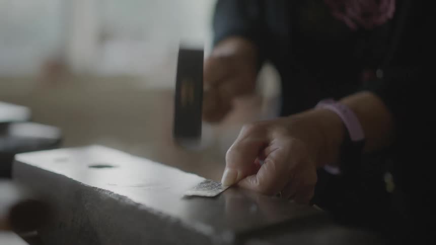 Hands of an elderly lady hammering a piece of metal into a concrete surface